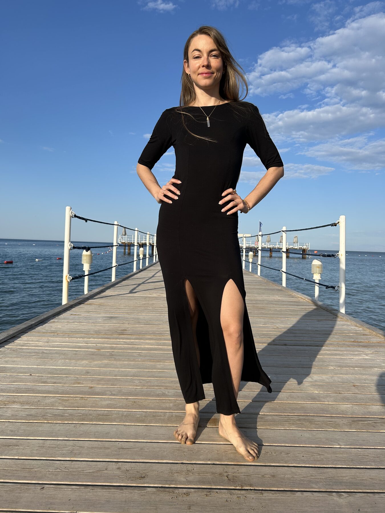 Coach standing on a pier above the sea, hands on hips, embodied and present